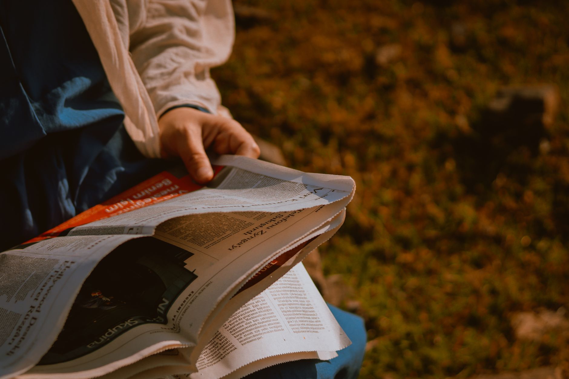 From above of crop unrecognizable person reading newspaper on green meadow in daylight — How to Maximize Your Bonuses at Barz